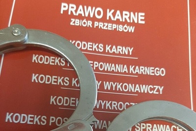 Widoczna część czerwonej okładki kodeksu karnego z położonymi na nim kajdankami