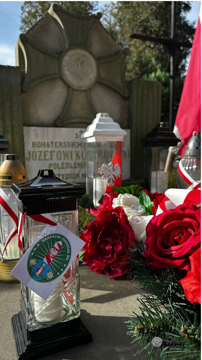 Grób Józefa Kustronia a na nim zapalony znicz z biało - czerwoną tasiemką i logiem Karpackiego Oddziału Straży Granicznej