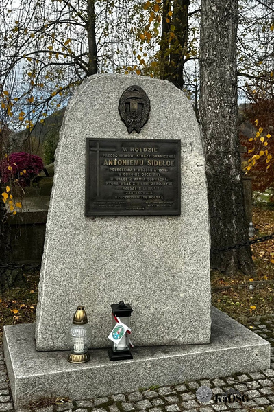 Grób Antoniego Sidełko a na nim zapalony znicz z biało - czerwoną tasiemką i logiem Karpackiego Oddziału Straży Granicznej