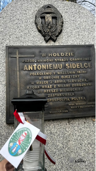 Grób Antoniego Sidełko a na nim zapalony znicz z biało - czerwoną tasiemką i logiem Karpackiego Oddziału Straży Granicznej