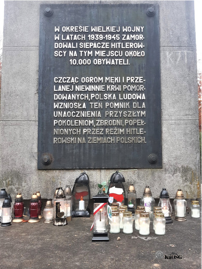 Zbliżenie na tablice pamiątkową na pomniku pod tablicą dużo zniczy, w tym nim zapalony  jeden znicz z biało - czerwoną tasiemką i logiem Karpackiego Oddziału Straży Granicznej