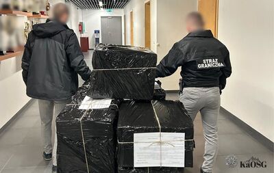 Dwóch funkcjonariuszy Straży Granicznej w korytarzu, oglądających stos dużych paczek owiniętych czarną folią, przewiązanych sznurkiem, z dokumentami przewozowymi na wierzchu.