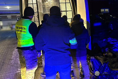 Na zdjęciu widać grupę ludzi przy samochodzie z otwartym tylnymi drzwiami. Jest ciemno, pora nocna.