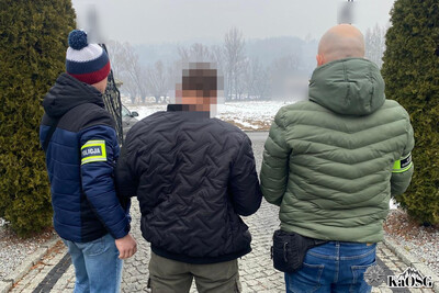 zatrzymany cudzoziemiec jest wyprowadzany przez nieumundurowanych dwóch funkcjonariuszy policji i straży granicznej z posesji na której przebywał