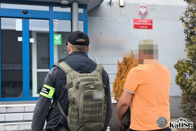zatrzymany cudzoziemiec w pomarańczowej koszulce idzie do wejścia do placówki sg w krakowie w  asyście nieumundurowanego funkcjonariusza straży granicznej