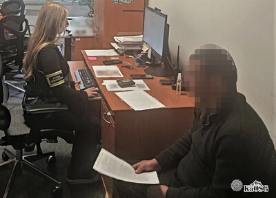 zatrzymany cudzoziemiec siedzi przy biurku, w rękach trzyma kartkę papieru. na komputerze pisze funkcjonariuszka