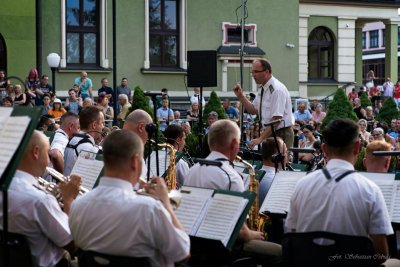 Na scenie występuje Orkiestra Reprezentacyjna Straży Granicznej, dyrygent dyryguje batutą, w tle publiczność.