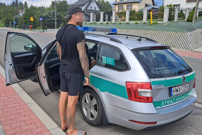 Mołdawianin nielegalnie w Polsce zatrzymany cudzoziemiec stoi obok pojazdu służbowego Straży Granicznej.