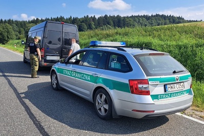 Mołdawianie nielegalnie w Polsce funkcjonariusz Straży Granicznej obok kierowca zatrzymanego busa sprawdzają zawartość bagażnika pojazdu, za nimi pojazd służbowy Straży Granicznej z włączonymi sygnałami świetlnymi