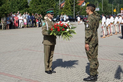 Miejsce uroczystości, plac przed pomnikiem partyzantów, Funkcjonariusz Karpackiego Oddziału Straży Granicznej składa kwiaty przed pomnikiem, w tle uczestnicy uroczystości.