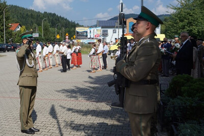 Miejsce uroczystości, plac przed pomnikiem partyzantów, Funkcjonariusz Karpackiego Oddziału Straży Granicznej oddaje honor po złożeniu kwiatów przed pomnikiem, w tle uczestnicy uroczystości.