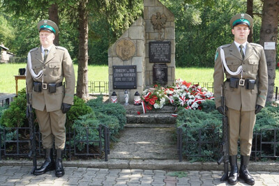 Dwóch funkcjonariuszy Karpackiego Oddziału Straży Granicznej wystawia posterunek honorowy przed pomnikiem partyzantów.