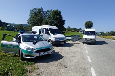 Mołdawianie nielegalnie w Polsce Pojazd służbowy straży granicznej, obok zatrzymane dwa pojazdy typu bus.
