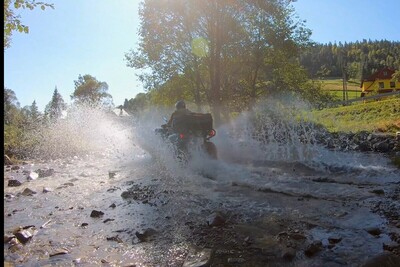 Funkcjonariusze KaOSG współdziałają i pomagają Funkcjonariusz Straży Granicznej przeprawiający się pojazdem służbowym typu quad przez górski potok. spod kół pojazdu rozpryskuje się woda.