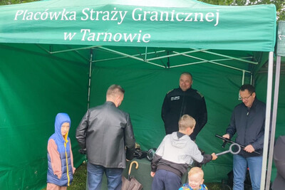 Promowali Straż Graniczną - PSG w Tarnowie Stoisko promocyjne Straży Granicznej. przy stoliku kilka osób oraz funkcjonariusz Straży Granicznej rozmawiający z nimi.