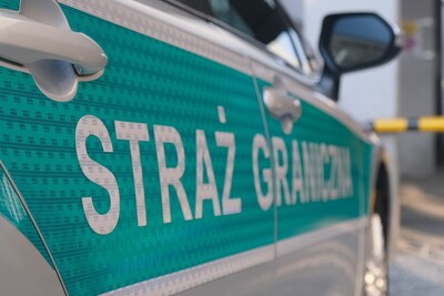 Azer nielegalnie w Polsce pojazd służbowy straży granicznej. widoczny napis na drzwiach pojazdu -  straż graniczna. w tle budynek.