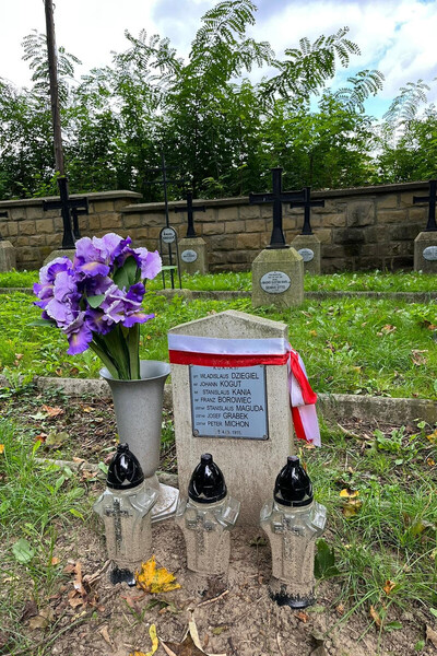 VIII akcja sprzątania cmentarzy z okresu I wojny światowej nagrobek poległych podczas I wojny światowej. nagrobek owinięty szarfą biało czerwoną pod nim trzy znicze , obok kwiaty.