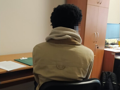 Zatrzymany obywatel Angoli siedzi tyłem przy biurku, na którym leżą kartki i teczka z dokumentami.