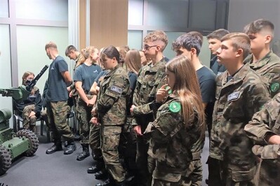 Uczniowie (około 20 osób) w mundurach w sali stoją i słuchają pogadanki.