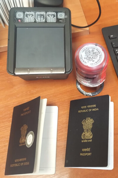Na biurku leżą dwa paszporty zatrzymanych obywateli Indii. Pieczęć okrągła z orzełkiem i napisem Komendant Placówki Straży Granicznej w Kielcach. Urządzenie do pobieranie odcisków palców.