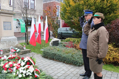 Funkcjonariuszka SG wraz z policjantem oddaje honor po złożeniu kwiatów pod pomnikiem Legionistów w Czarnym Dunajcu. Powiewają biało-czerwone flagi. W tle budynki mieszkalne.
