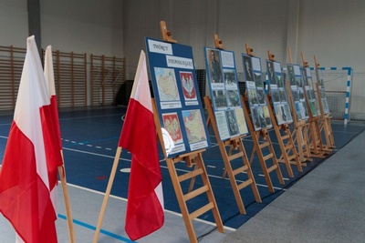 Hala widowiskowo-sportowa w Korzennej. Na dużych sztalugach umieszczona wystawa pod tytułem Twórcy niepodległej. Po lewej trzy biało-czerwone flagi.