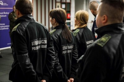 Pomieszczenie strzelnicy. Drużyna funkcjonariuszy Straży Granicznej z Kielc w czarnych polarach stoi tyłem.