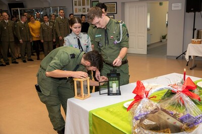 Spotkania wigilijne w Karpackim Oddziale Straży Granicznej harcerze zapalający świecę, która położona jest na stole z opłatkami.