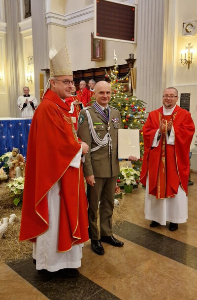 Komendant KaOSG wyróżniony przez Biskupa Polowego Komendant Karpackiego Oddziału Straży Granicznej pozujący do zdjęcia wraz z Biskupem Polowym z wręczonym odznaczeniem. uroczystość odbywa się w kościele.