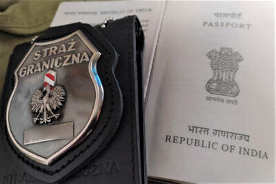 Otwarty paszport hinduski. Obok leży metalowa odznaka Straży Granicznej