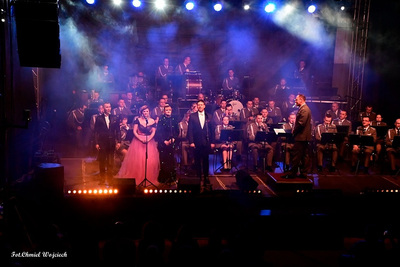 Sala koncertowa. Soliści - dwie kobiety i dwóch mężczyzn - stoją na scenie. Za nimi muzycy orkiestry reprezentacyjnej straży granicznej obok dyrygent.