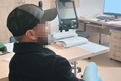 Zatrzymany obywatel Maroka siedzi przy biurku ma zapikselizowaną twarz. W tle stoją dwa biurka, na jednym z nich monitor komputera, a obok krzesło biurowe
