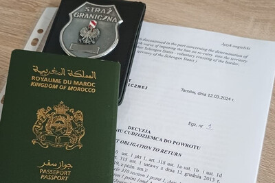 Na biurku leży decyzja o zobowiązaniu cudzoziemca do powrotu. Na niej odznaka funkcjonariusza sg i paszport obywatela maroko