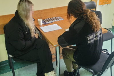 Zatrzymana Białorusinka siedzi przy stoliku. Obok niej siedzi funkcjonariuszka SG, która uzupełnia dokumentację z zatrzymania.