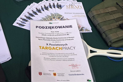 Podziękowanie od organizatorów dla Karpackiego Oddziału Straży granicznej oraz Placówki straży granicznej w Krakowie za udział w targach pracy. jest to kartka  formatu a4 położona na stoisku , pod nią znajduje się tarczka stop oraz broszurki informacyjne o Straży granicznej.