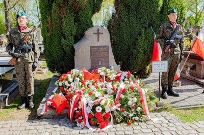 warta honorowa wystawiona przez młodzież zs strzelca pełni wartę honorową przy symbolicznym grobie sybiraków na cmentarzu w nowym sączu. przed pomnikiem leży kilka wieńców biało-czerwonych kwiatów i znicze