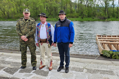 generał Jopek stoi nad brzegiem Dunajca w towarzystwie prezesa stowarzyszenia flisaków pienińskich oraz jednego z flisaków. po prawej stronie zawodowana łódź flisacka