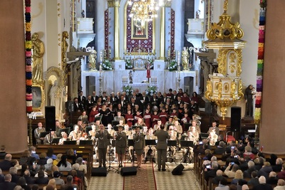 Wnętrze bazyliki w limanowej. w prezbiterium muzycy orkiestry oraz śpiewająca trójka wokalistów orkiestry oraz dyrygent koncertu słucha licznie zgromadzona publiczność