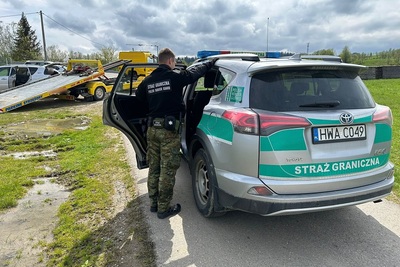 Radiowóz straży granicznej, w środku zatrzymany Polak, przed pojazdem laweta, która przyjechała po  zabezpieczony samochód zatrzymanego mężczyzny