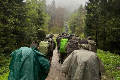 Zdobyli Wojskową Odznakę Górską 21 Brygady Strzelców Podhalańskich uczestnicy kwalifikacji maszerujący w terenie górskim. otoczenie to las. uczestnicy idą po drodze leśnej. pada deszcz.