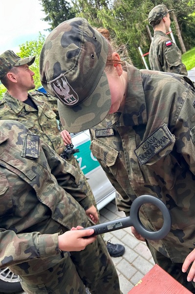 Jedna z uczennic w mundurze przy użyciu wykrywacza do metali obszukuje koleżankę