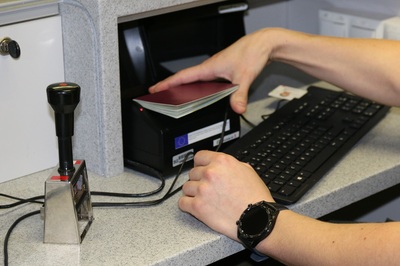 funkcjonariusz straży granicznej skanujący paszport osoby sprawdzanej. widoczny jest również stempel kontrolerski. na ręce funkcjonariusza znajduje się czarny zegarek.