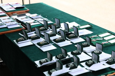 stolik na którym jest obrus w kolorze zielonym. Na stole ułożone są medale oraz odznaczenia które zostaną wręczone podczas uroczystości.