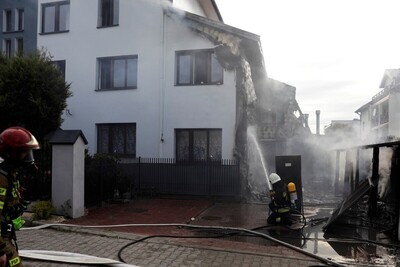 Widok ściany budynku po pożarze. Dwóch strażaków wykonuje czynności gaśnicze.