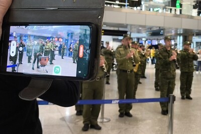 muzycy orkiestry reprezentacyjnej straży granicznej podczas kręcenia flash moba na krakowskim lotnisku. obserwują ich zebrani podróżni. używają telefonów aby zrejestrować występ orkiestry reprezentacyjnej straży granicznej.