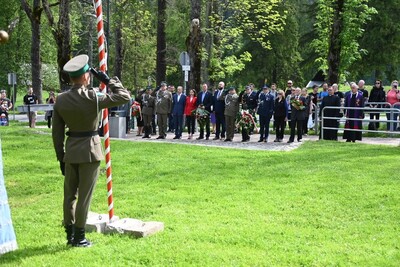 na pierwszym planie funkcjonariusz straży granicznej oddający honor przed masztem na którym zawieszona jest flaga Polski. w tle uczestnicy uroczystości również oddają honor lub stoją na baczność podczas odśpiewanego hymnu Polski.