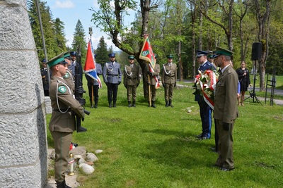 przedstawiciele służb mundurowych składają wieniec pod Pomnikiem. na pierwszym planie stoi zastępca komendanta z placówki straży granicznej w Zakopanem. przy pomniku stoją dwaj funkcjonariusze z bronią długa pełniąc wartę honorową.