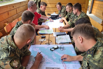 Funkcjonariusze KaOSG i instruktorzy GOPR siedzą przy stole z rozłożonymi mapami