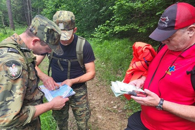 Dwóch funkcjonariuszy KaOSG i instruktor GPPR w terenie leśnym wytyczają azymut na podstawie mapy i kompasu.
