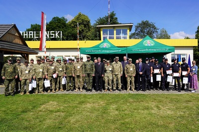 wszyscy zebrani na uroczystości, czyli żołnierze ukraińscy i ich trenerzy, przedstawiciele karpackiego oddziału straży granicznej i komisji europejskiej oraz psy służbowe. wszyscy pozują do wspólnej fotografii.